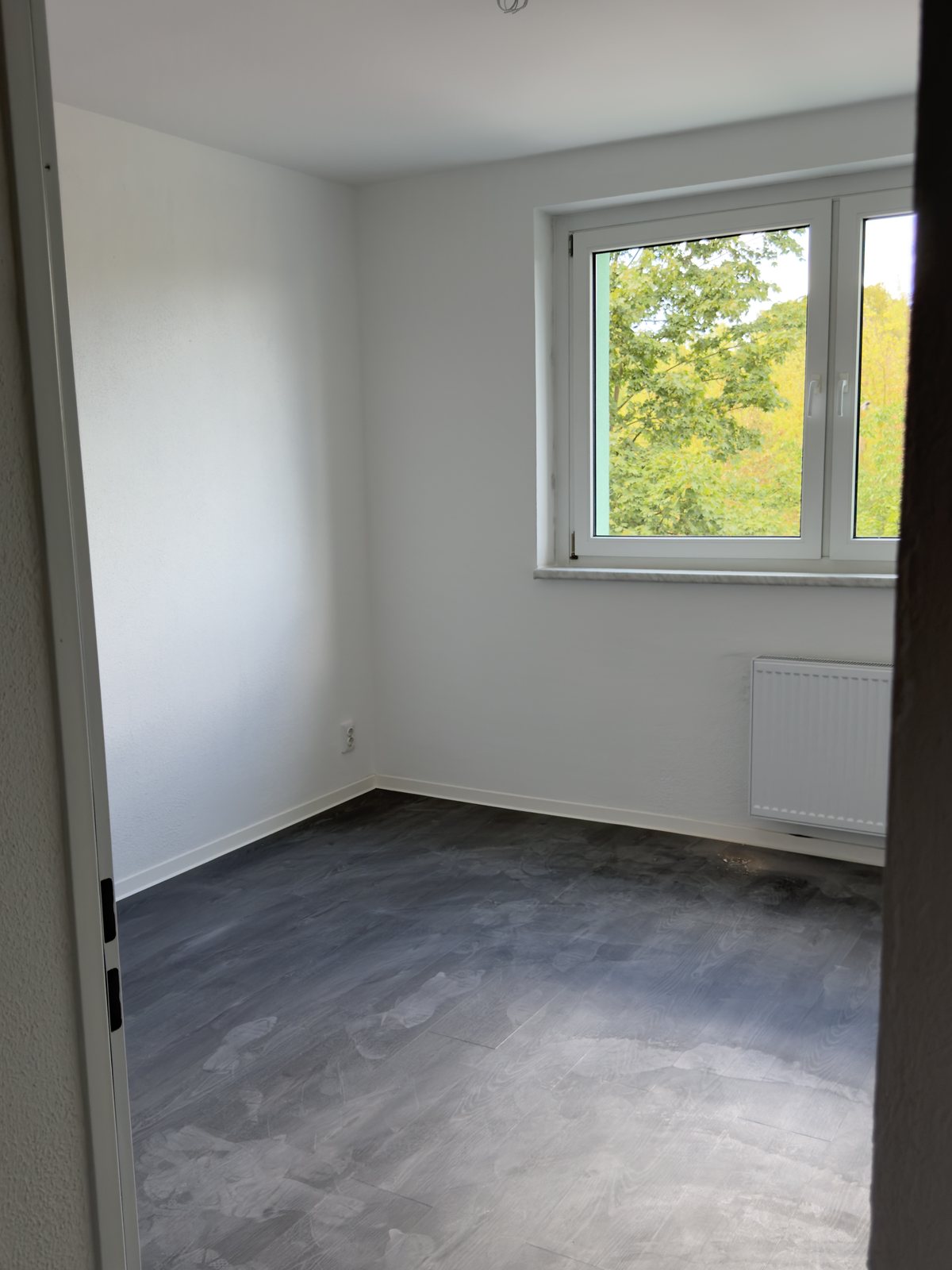 Zweites Zimmer nach der Sanierung mit hellen Wänden und dunklem Boden