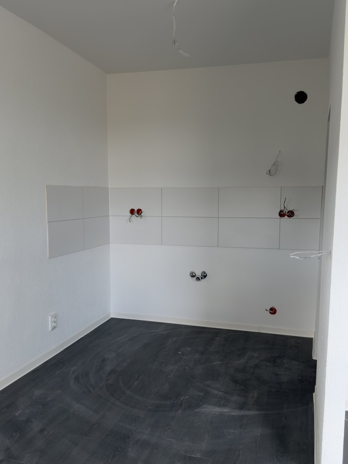 Fertige Küche mit weißem Fliesenspiegel, Anschlüssen und dunklem Designboden