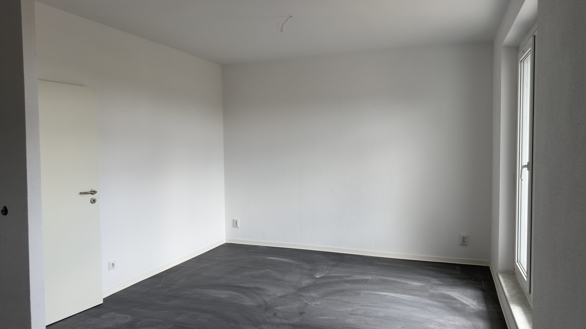 Fertiges Wohnzimmer mit weißen Wänden, dunklem Designboden und eingesetzter Zimmertür