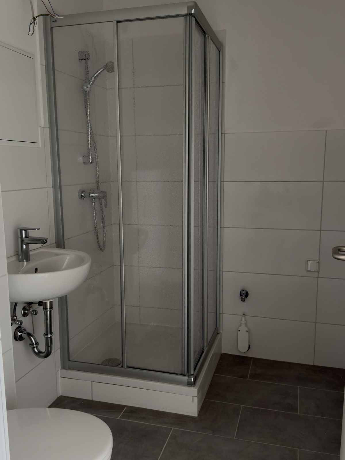 Fertiges Bad mit neuer Eckdusche, Waschbecken, Wand-WC und grauen Bodenfliesen