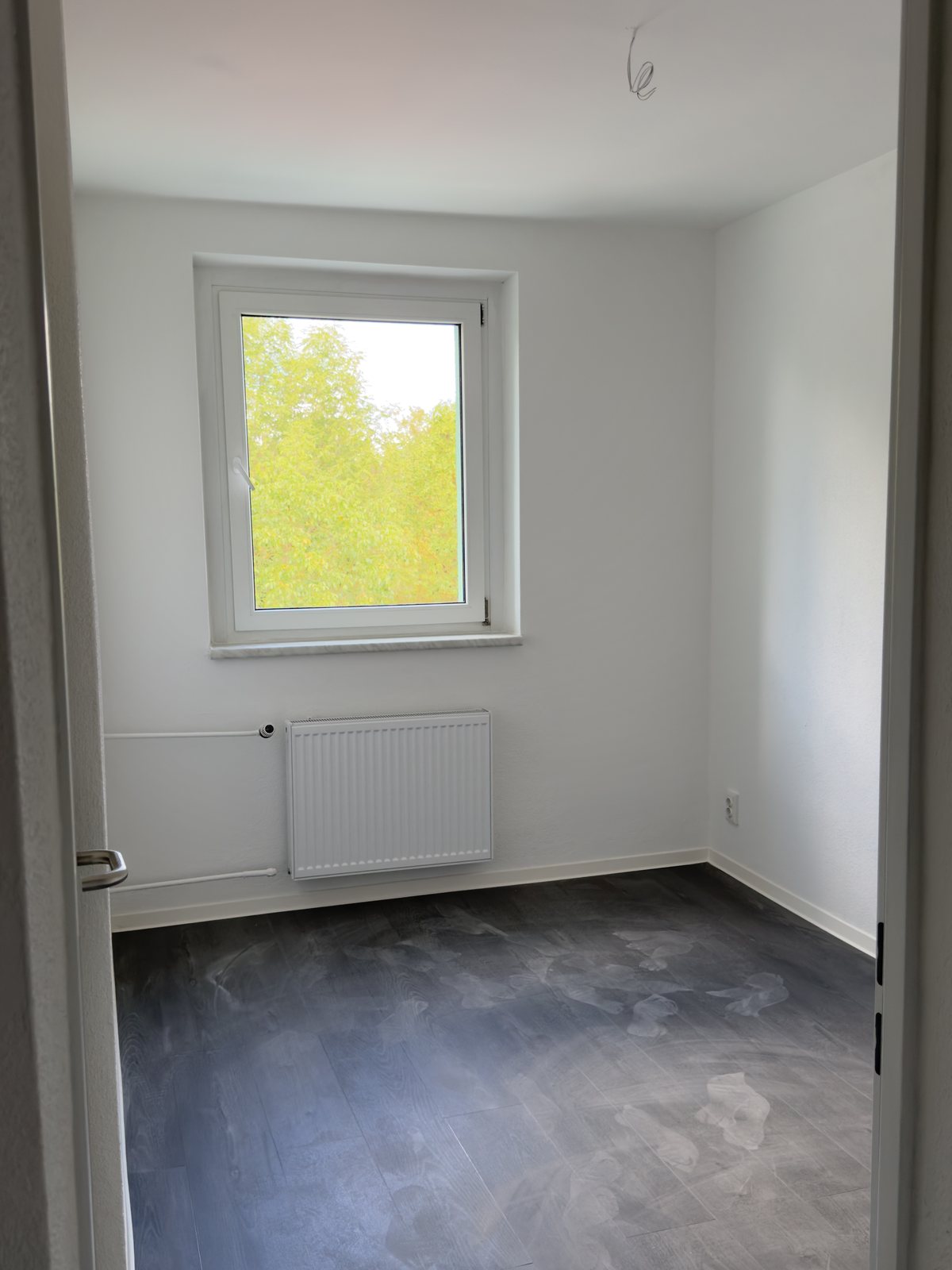 Fertiges Zimmer mit weißen Wänden, dunklem Designboden und Heizkörper unter dem Fenster