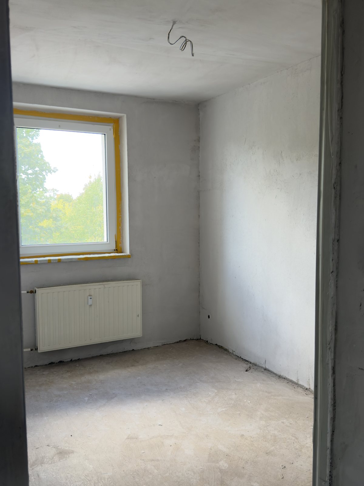 Zimmer im Rohbau mit unverputzten Wänden und blankem Estrich
